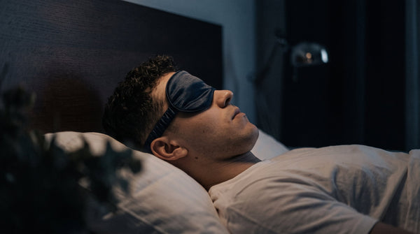 Junger Mann mit Schlafmaske im Bett entspannt durch das PHAIZE Magnesium Spray.