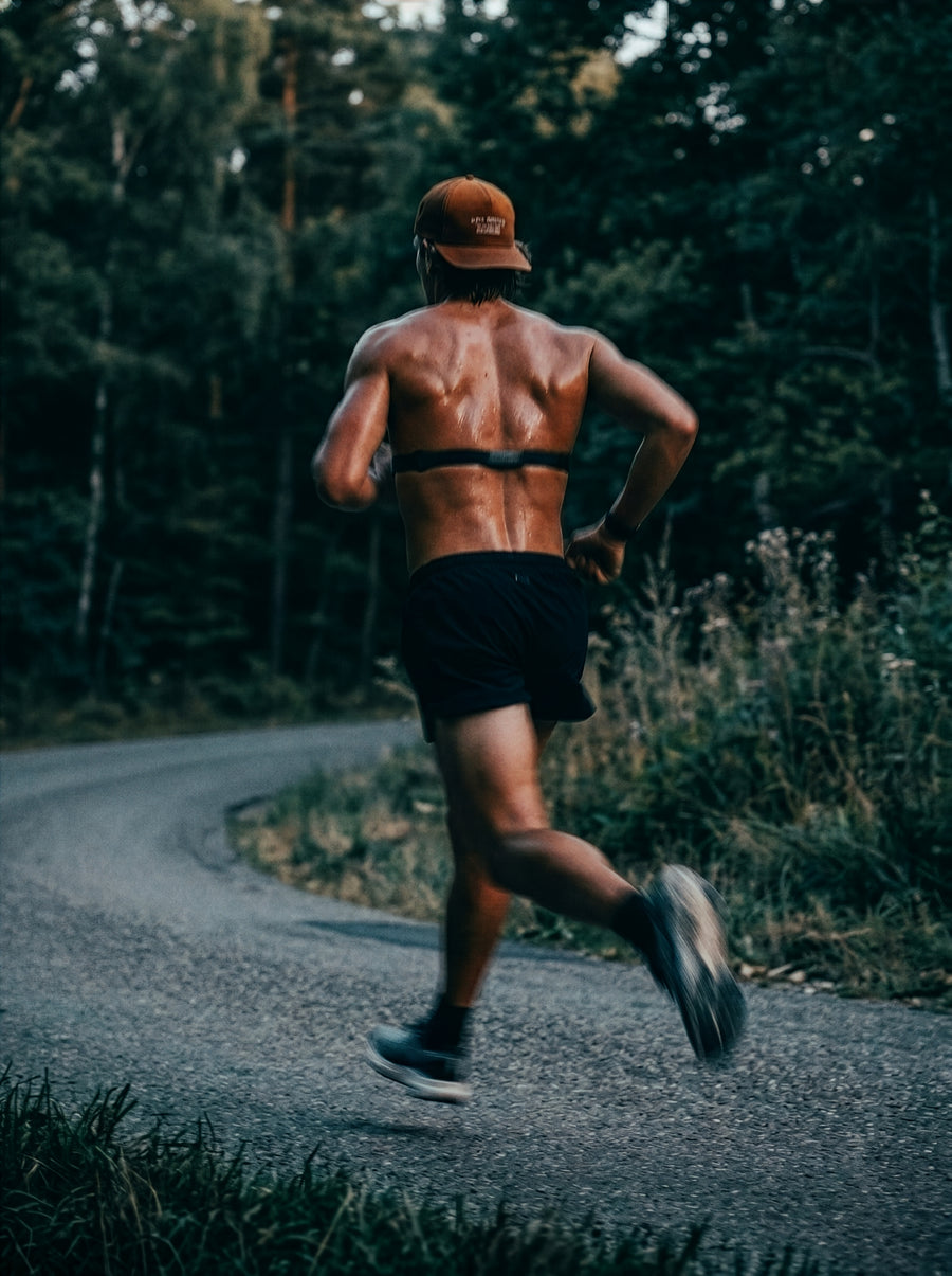 Leistungssportler mit Pulsgurt beim Sprint auf einer Waldstraße. Kompromisslose Muskelregeneration nach dem Training durch PHAIZE Magnesium spray.